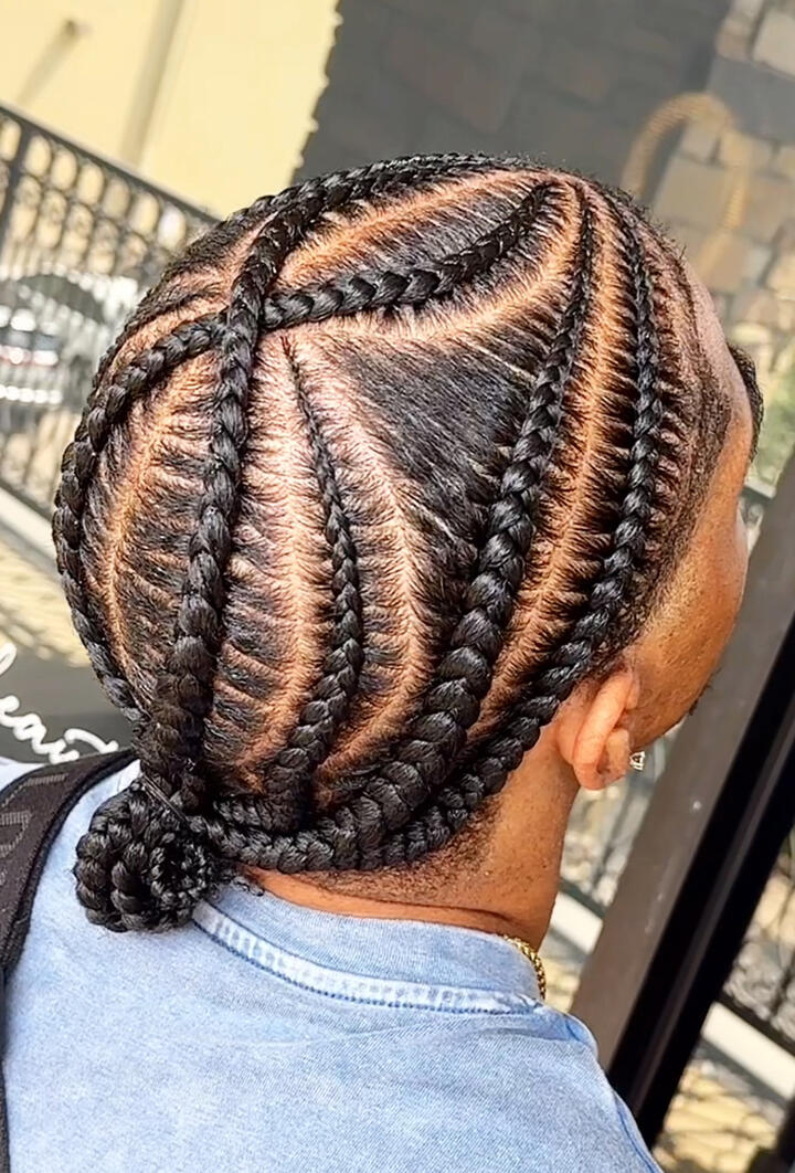 A close-up of a man with a fresh haircut and groomed beard, wearing a barber cape inside a modern barbershop.