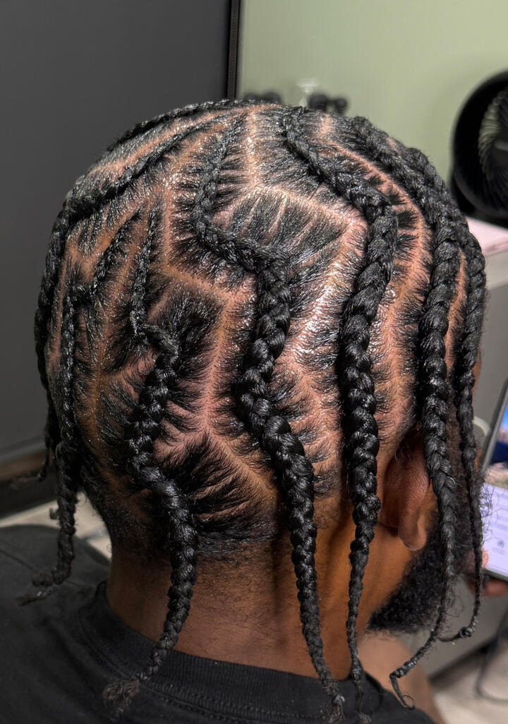 A close-up of a man with a fresh haircut and groomed beard, wearing a barber cape inside a modern barbershop.